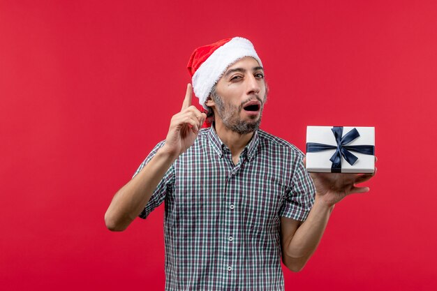 Vue de face du jeune homme tenant un cadeau de Noël sur rouge