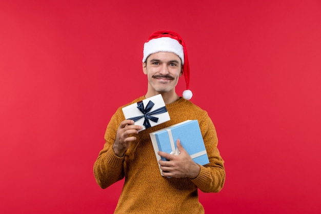 Vue de face du jeune homme tenant des cadeaux sur le mur rouge