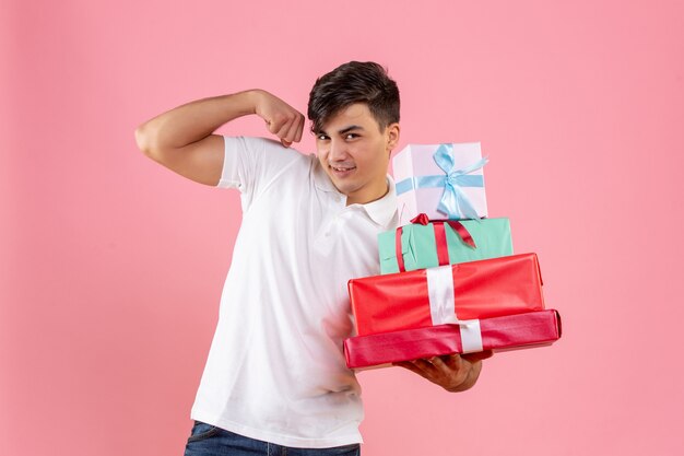 Vue de face du jeune homme tenant des cadeaux de Noël fléchissant sur le mur rose