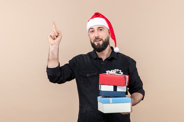 Vue de face du jeune homme tenant des cadeaux de Noël sur le mur rose