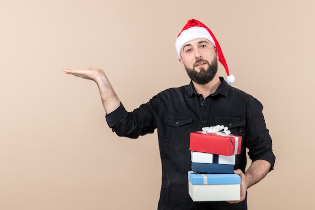 Vue de face du jeune homme tenant des cadeaux de Noël sur le mur rose