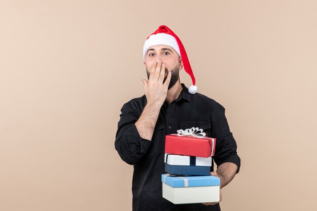 Vue de face du jeune homme tenant des cadeaux de Noël sur le mur rose