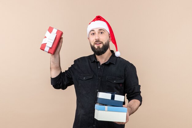 Vue de face du jeune homme tenant des cadeaux de Noël sur le mur rose