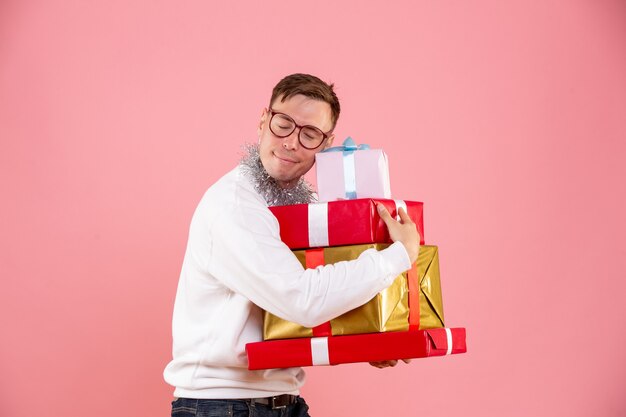 Vue de face du jeune homme tenant des cadeaux de Noël sur un mur rose