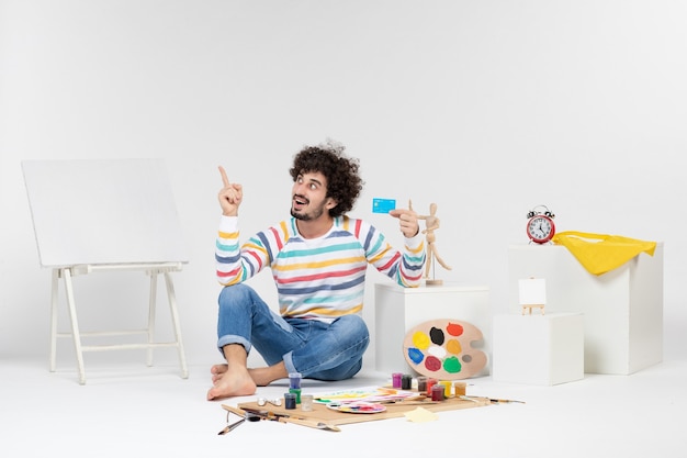 Photo gratuite vue de face du jeune homme tenant une carte bancaire sur un mur blanc