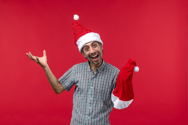 Vue de face du jeune homme tenant une casquette de Noël rouge sur le mur rouge