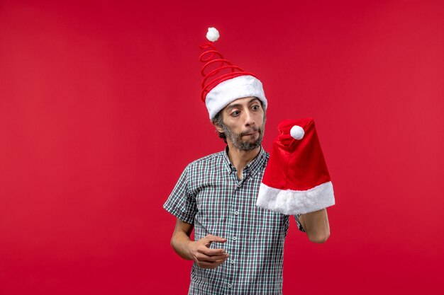 Vue de face du jeune homme tenant le chapeau de Noël sur le mur rouge