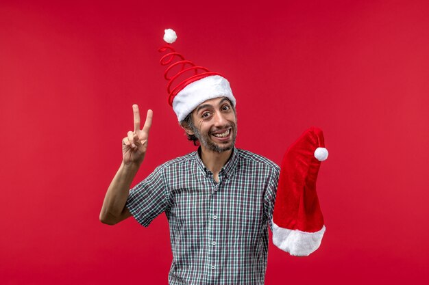 Vue de face du jeune homme tenant le chapeau de Noël sur le mur rouge