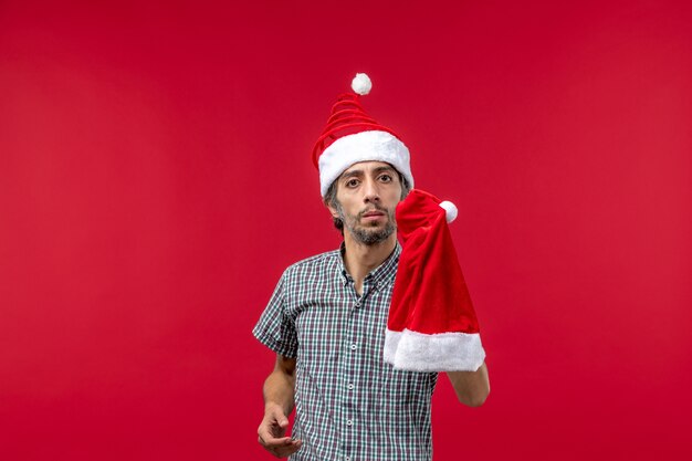 Vue de face du jeune homme tenant le chapeau de Noël sur le mur rouge