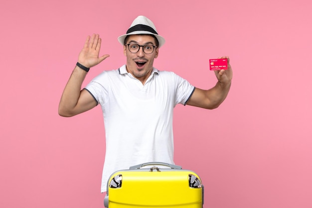 Vue de face du jeune homme tenant émotionnellement une carte bancaire en vacances sur un mur rose