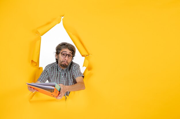 Vue de face du jeune homme tenant des fichiers sur un mur jaune