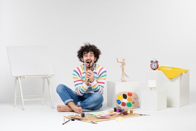 Vue de face du jeune homme tenant des glands pour dessiner sur un mur blanc