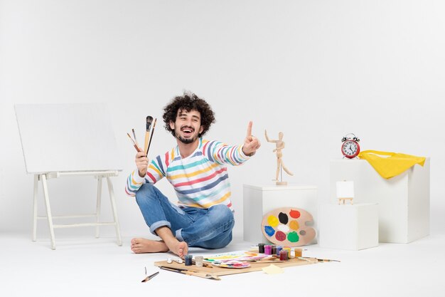 Vue de face du jeune homme tenant des glands pour dessiner sur un mur blanc