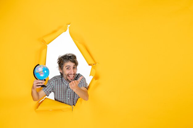 Vue de face du jeune homme tenant un globe terrestre sur un mur jaune