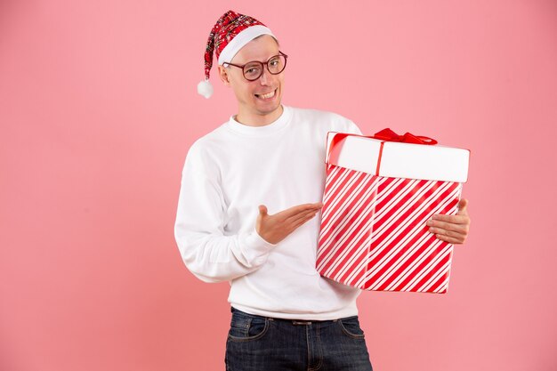 Vue de face du jeune homme tenant un gros cadeau sur le mur rose