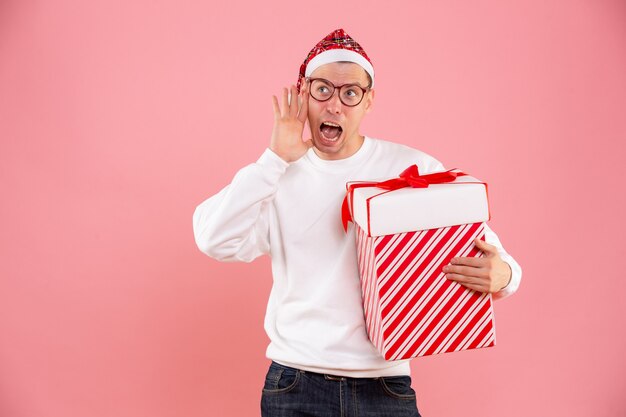 Vue de face du jeune homme tenant un gros cadeau sur le mur rose