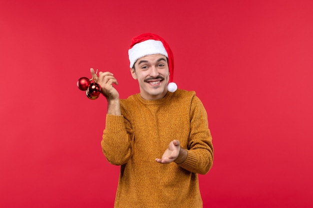 Vue de face du jeune homme tenant des jouets en plastique sur le mur rouge