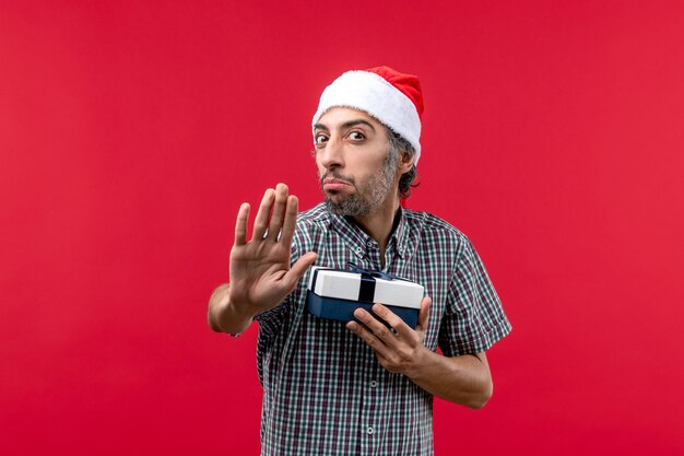 Vue de face du jeune homme tenant un petit cadeau de Noël sur le rouge