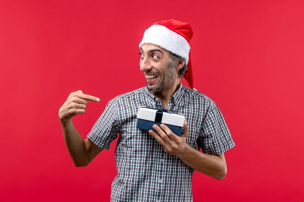 Vue de face du jeune homme tenant un petit cadeau de Noël sur le rouge