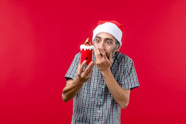 Vue de face du jeune homme tenant un petit jouet de vacances sur le rouge