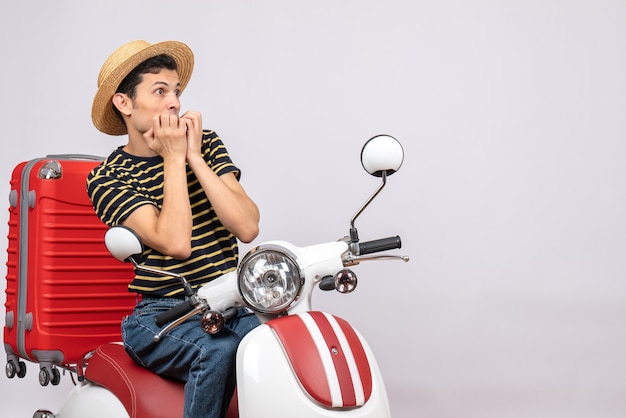 Vue de face du jeune homme terrifié avec un chapeau de paille sur un cyclomoteur