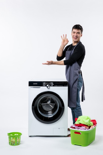 Vue de face du jeune homme avec des vêtements sales et une laveuse sur un mur blanc