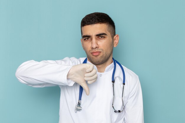 Vue de face du jeune médecin de sexe masculin en costume blanc avec stéthoscope bleu montrant un signe différent