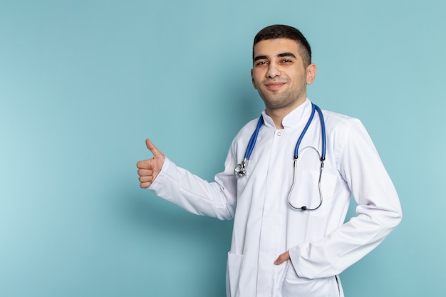 Vue de face du jeune médecin de sexe masculin en costume blanc avec stéthoscope bleu posant