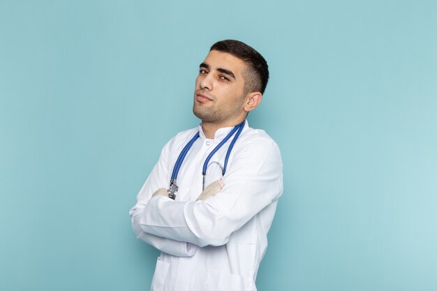 Vue de face du jeune médecin de sexe masculin en costume blanc avec stéthoscope bleu posant