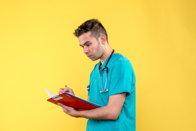 Vue de face du jeune médecin de sexe masculin écrit des notes sur le mur jaune