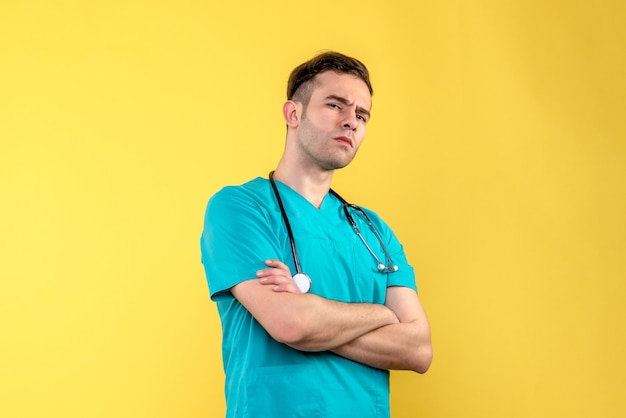 Vue de face du jeune médecin de sexe masculin pensant au mur jaune