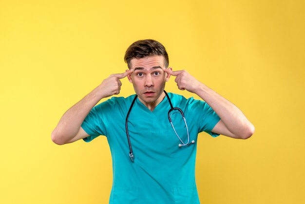 Vue de face du jeune médecin de sexe masculin posant sur un mur jaune