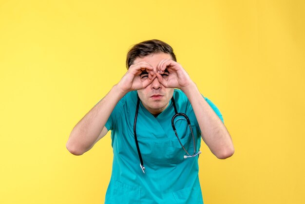Vue de face du jeune médecin de sexe masculin regardant à travers les doigts sur le mur jaune