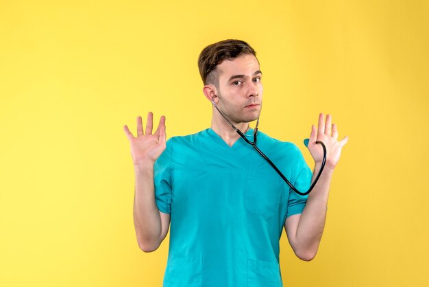 Vue de face du jeune médecin de sexe masculin avec stéthoscope sur mur jaune