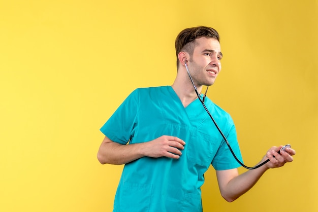 Vue de face du jeune médecin de sexe masculin avec stéthoscope sur mur jaune