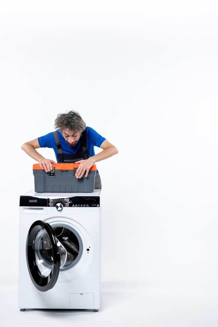 Photo gratuit vue de face du jeune réparateur debout derrière le sac d'outils d'ouverture de machine à laver sur un mur blanc