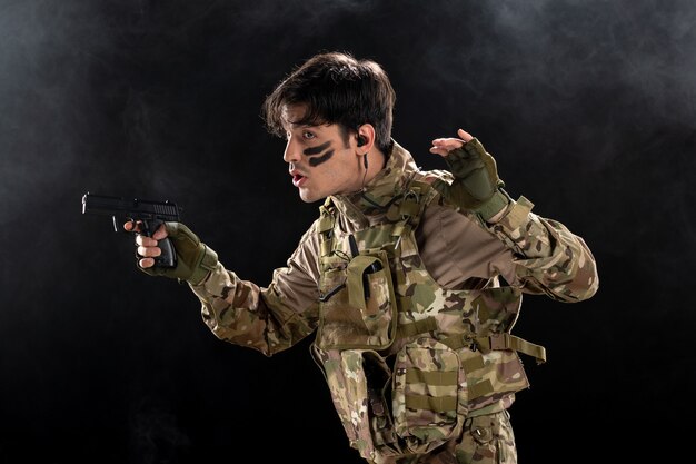 Vue de face du jeune soldat avec arme en camouflage sur mur noir