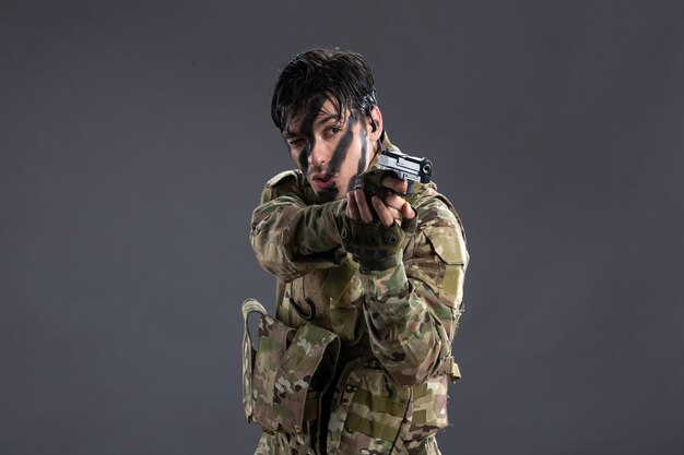 Vue de face du jeune soldat en camouflage visant le pistolet sur le mur sombre