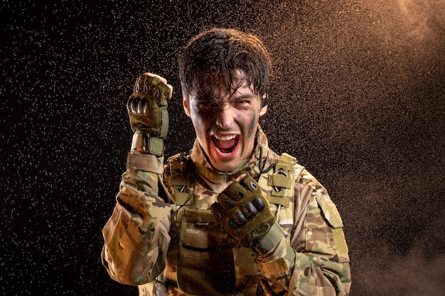 Vue de face du jeune soldat hurlant en uniforme sur un mur noir