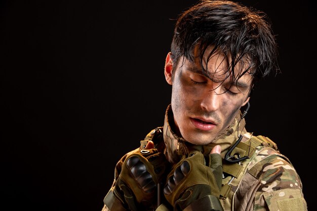 Vue de face du jeune soldat en uniforme sur un mur sombre