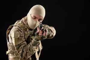 Photo gratuite vue de face du jeune soldat en uniforme visant le pistolet sur mur noir