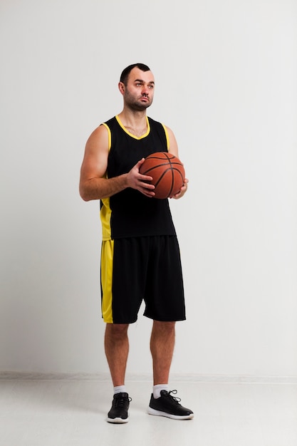 Vue de face du joueur de basket-ball détendu posant avec ballon