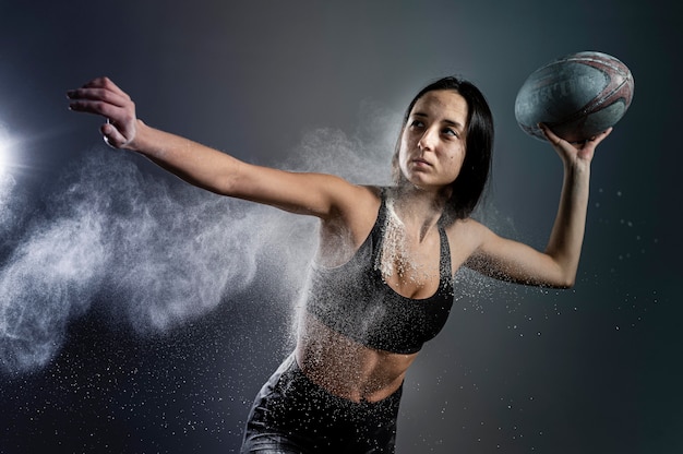 Vue de face du joueur de rugby féminin athlétique tenant le ballon avec de la poussière