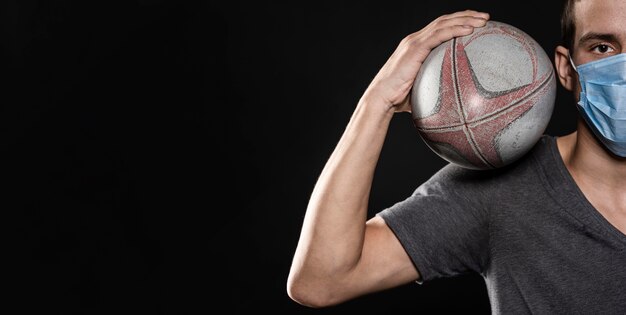 Vue de face du joueur de rugby masculin avec masque médical et ballon