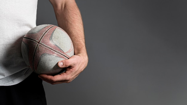 Vue de face du joueur de rugby masculin tenant le ballon à côté de la hanche avec copie espace