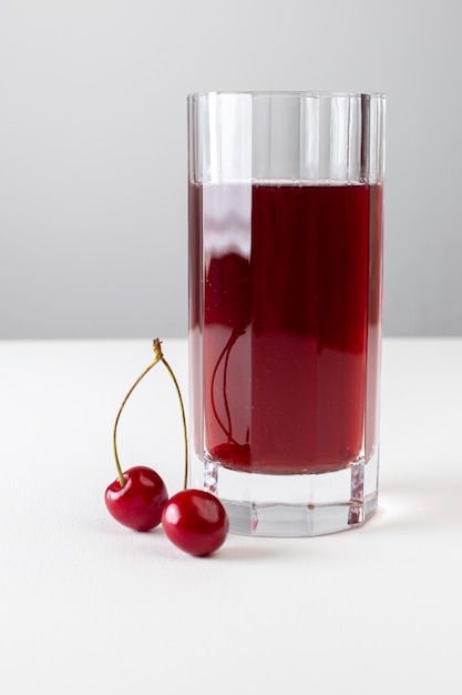 Vue de face du jus de cerise à l'intérieur d'un long verre sur la surface blanche