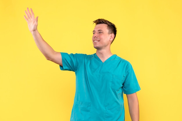 Vue de face du médecin de sexe masculin en agitant avec sourire sur mur jaune