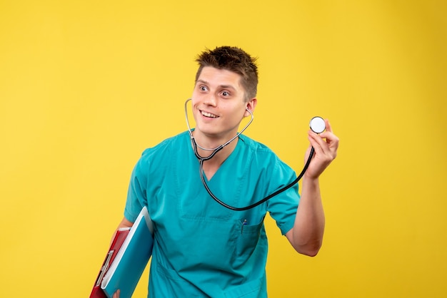 Vue de face du médecin de sexe masculin en costume médical avec analyse et stéthoscope sur mur jaune