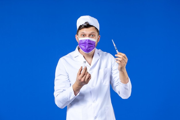 Vue de face du médecin de sexe masculin en costume médical et masque avec injection et vaccin sur bleu