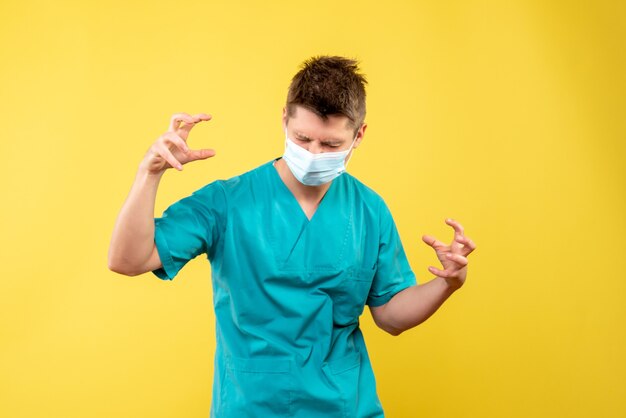 Vue de face du médecin de sexe masculin en costume médical et masque stérile sur mur jaune